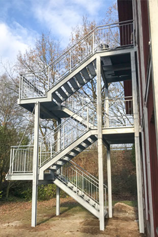 Gegenläufige Podesttreppe in feuerverzinktem Stahl als Fluchttreppe über zwei Etagen